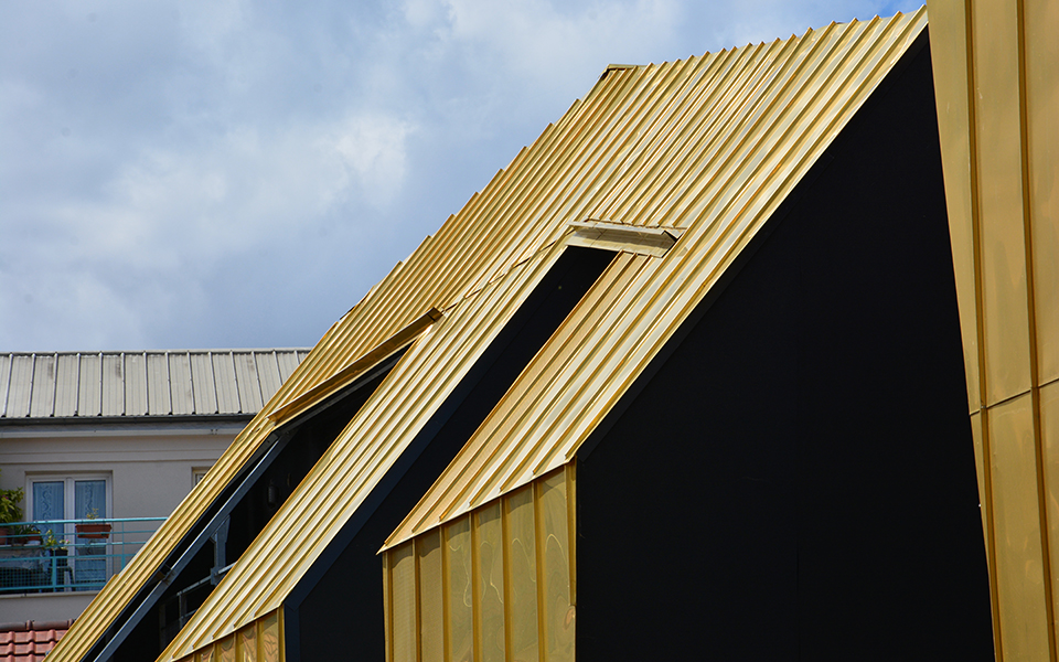 détail de toiture et façade en cuivre doré à joints debouts avec chéneau jonction avec un mur noir en enduit ventilé